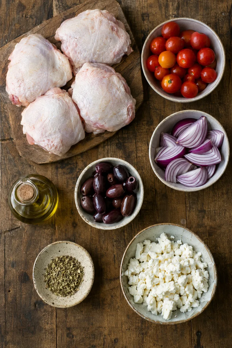Ingredients laid out: chicken thighs, cherry tomatoes, red onion, kalamata olives, olive oil, oregano and feta