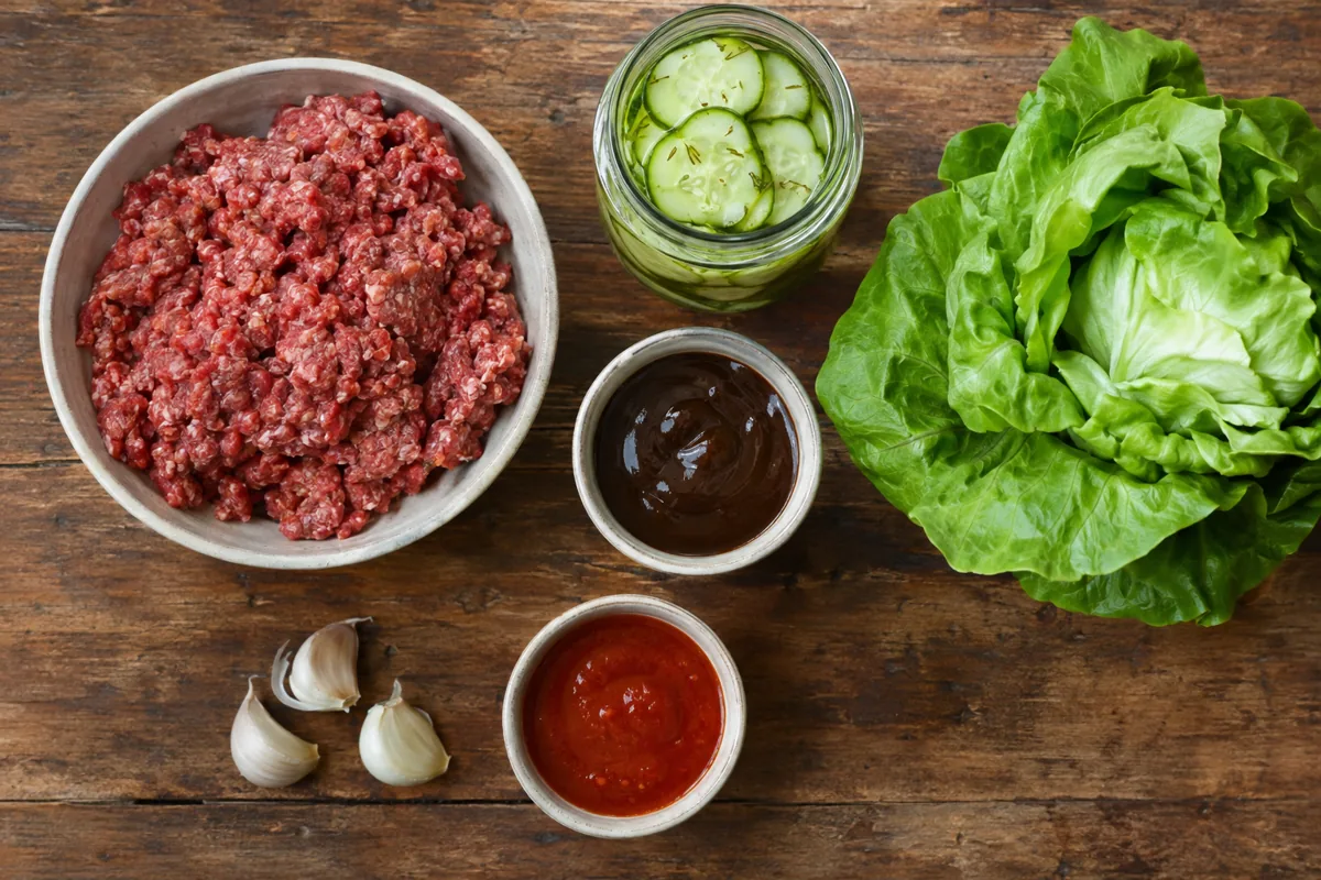 Ingredients laid out: ground beef, garlic, hoisin sauce, sriracha, butter lettuce and quick pickled cucumbers